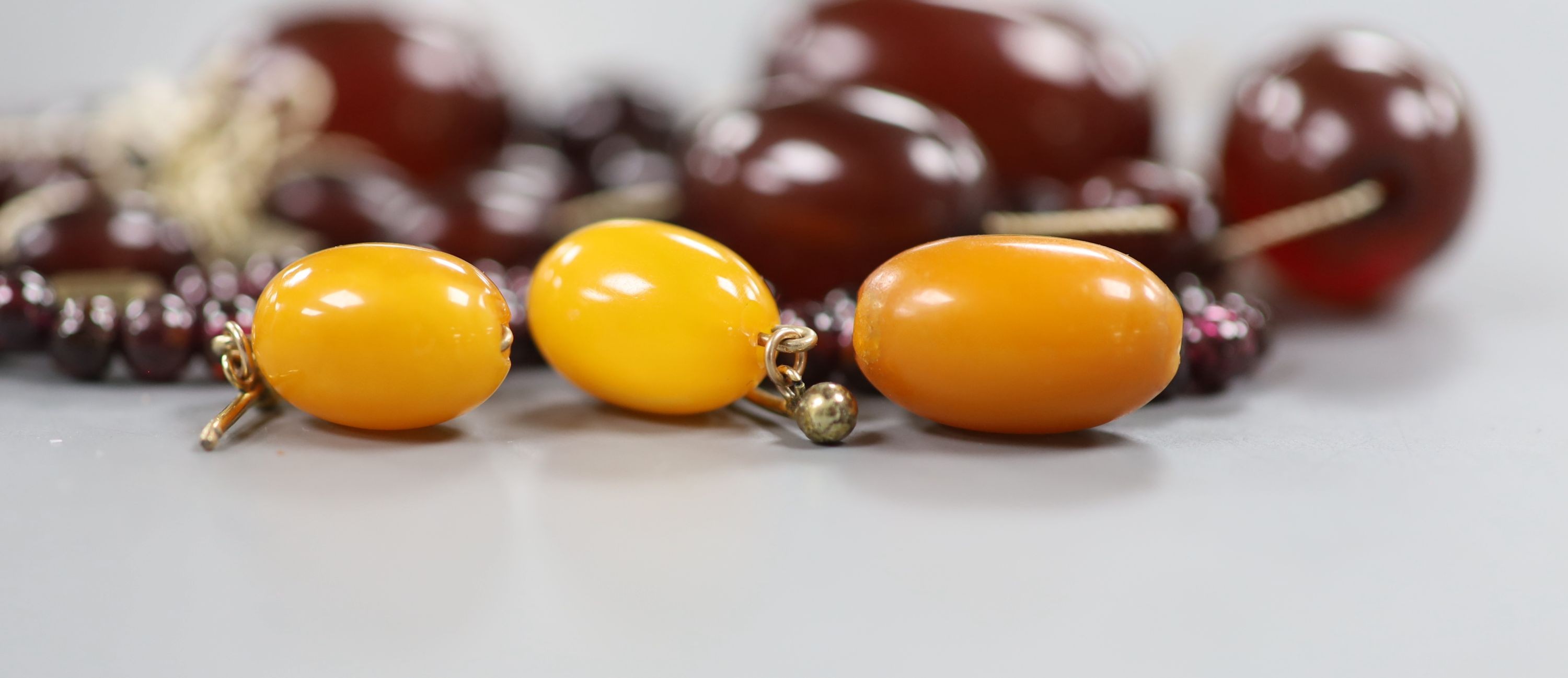 A pair of amber earrings, some loose simulated amber beads and a garnet bead necklace.